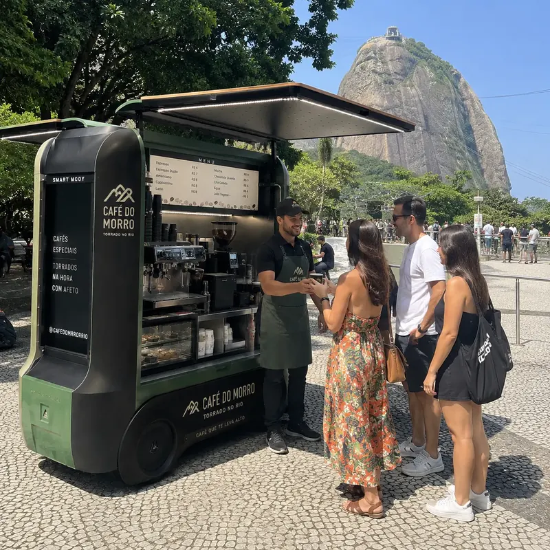 Quiosque de café verde e preto num calçadão com o Pão de Açúcar ao fundo